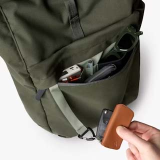 在一个橄榄色 Belroy Classic 卷顶背包的前袋旁,一只手拿着钥匙圈上的浅棕色钥匙环,背包里的物品清晰可见。 在一个橄榄色 Belroy Classic 卷顶背包的前袋旁,一只手拿着钥匙圈上的浅棕色钥匙环,背包里的物品清晰可见。